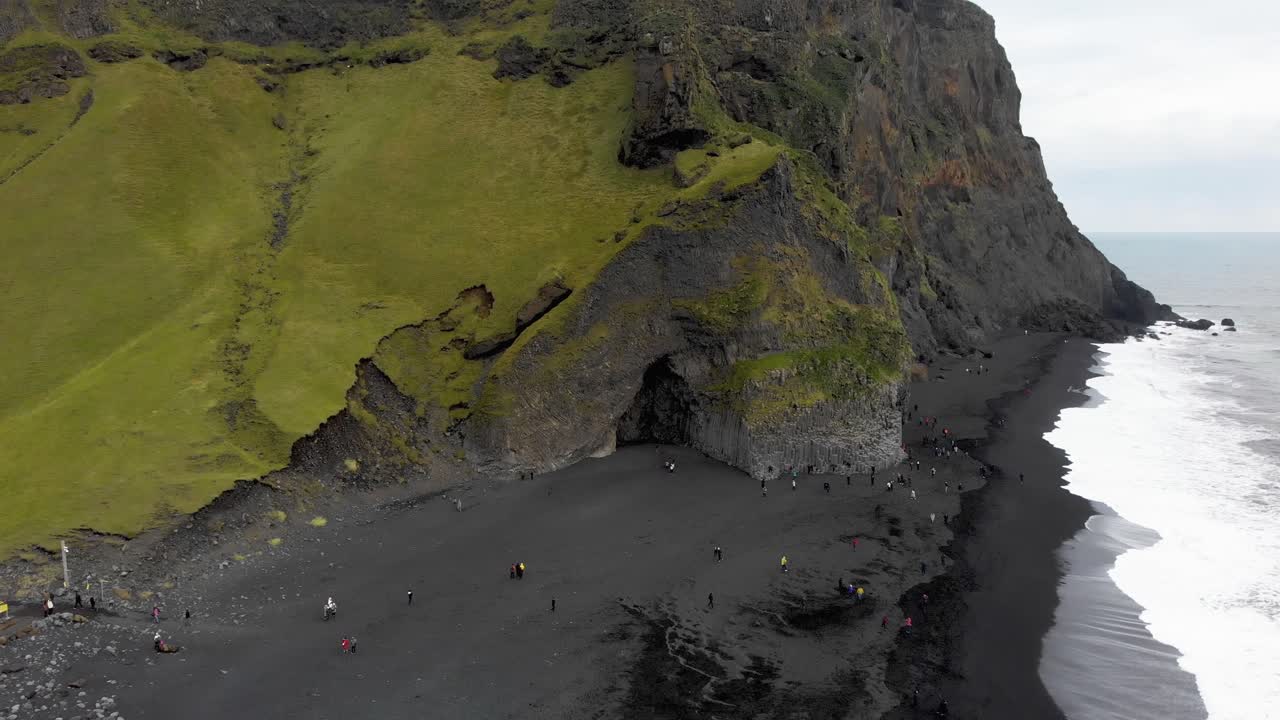 turistas que visitan la playa de arena negra de reynisfjara con cueva de roca, islandia