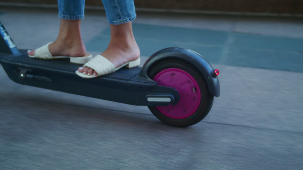 스쿠터에서 알려지지 않은 여성의 발이 가 ⁇ 습니다. 여성의 다리는 전기 자전거에 서 있습니다.