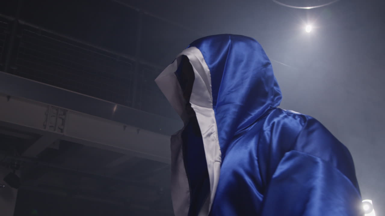 파란 망토를 입은 권투 선수가 어두운 권투 링에 서 있습니다.