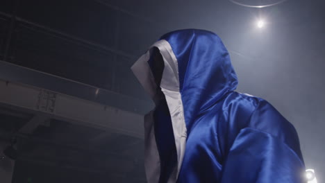 un boxeador con una túnica azul está en un ring de boxeo oscuro.