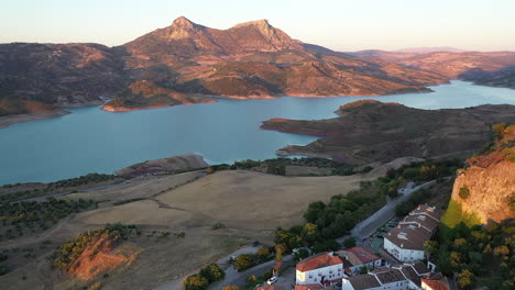 AERIAL---Zahara-de-la-Sierra-and-its-lake,-Cadiz,-Spain,-wide-shot-lowering