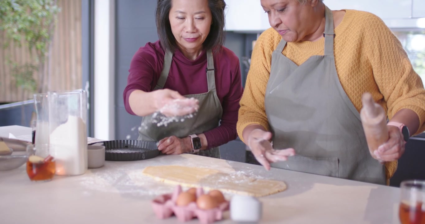 Berbagai wanita meletakkan adonan, menggulung adonan kue, dan menaburkan tepung di meja dapur untuk kue tart dengan penggilas adonan.