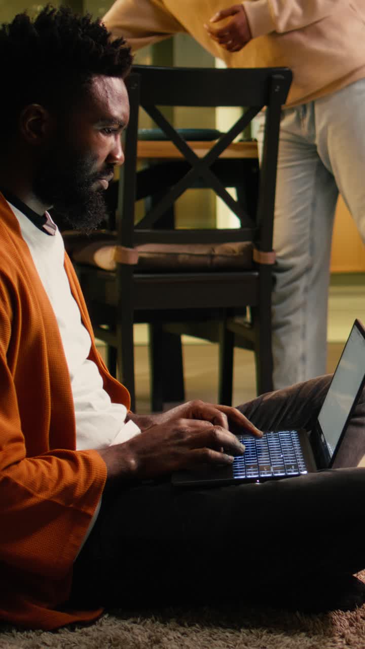 Vertical Video African american person, relaxing with laptop, sitting on the floor at home