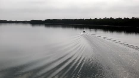 Calm-river-with-a-single-boat-creating-ripples-on-the-water-surface,-A-peaceful-journey-in-a-serene-setting