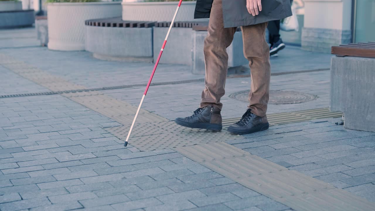 hombre con discapacidad visual está caminando en una baldosa de advertencia táctil con la ayuda de su bastón. superficie de advertencia detectable para los discapacitados visuales al aire libre en la ciudad.