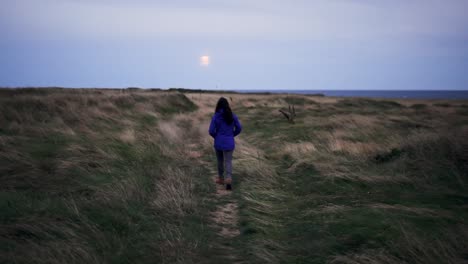 anonymous female hiker walking on dry terrain near sea in evening