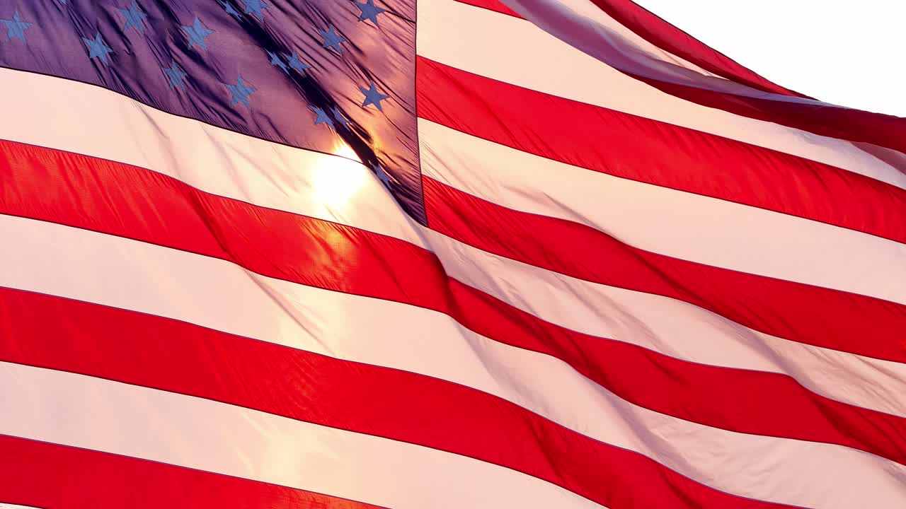 Closeup of American flag illuminated by sunset with golden highlights and fluttering in wind