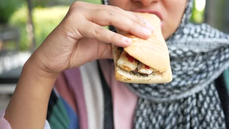 a woman wearing a hijab eats a delicious sandwich