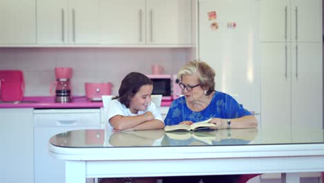 Anciana-Leyendo-Un-Libro-Con-Su-Nieta-En-La-Cocina-Ligera-De-Casa