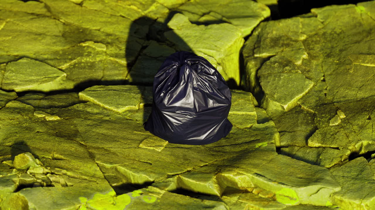 Black trash bag resting on rocky green surface in natural setting