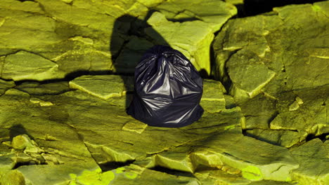 black trash bag resting on rocky green surface in natural setting