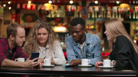 multi-ethnic couples sitting in a cafe show photos to each other and laugh