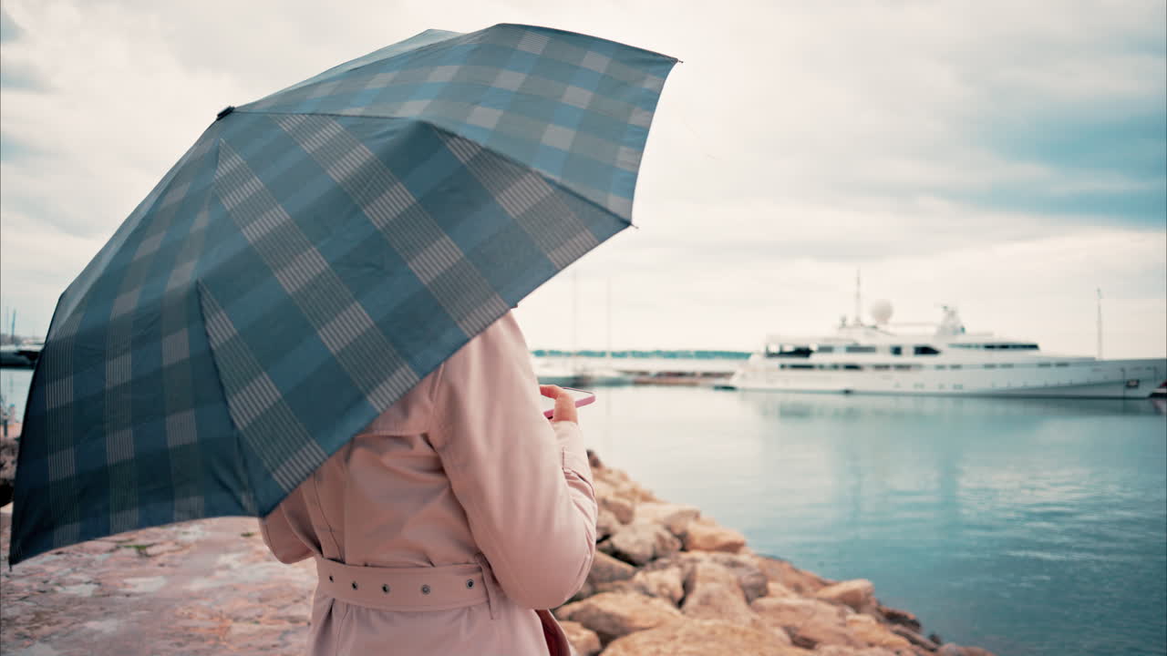 Woman wearing a trench coat looking at the sea in the rain in Cannes, France