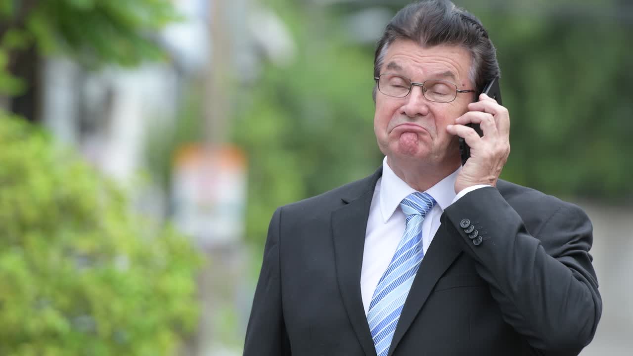 Senior handsome businessman talking on the phone in the streets outdoors