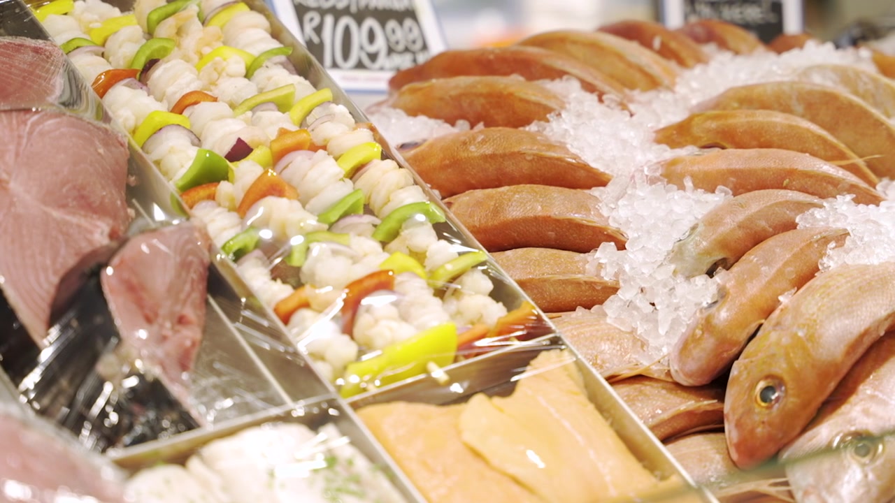 明るい小売店の陳列ケースの中で、氷の上に置かれた丸ごとの魚が色とりどりのシーフードと野菜の串焼きの隣に並んでいる