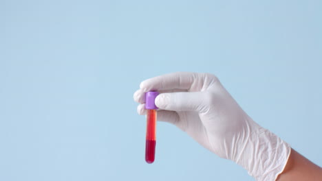 mano con guante médico sosteniendo una muestra de sangre sobre fondo azul con espacio de copia, cámara lenta