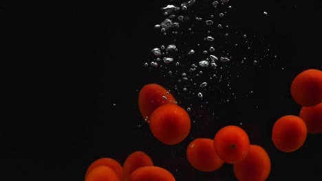 many tomatoes falling into water on the black background