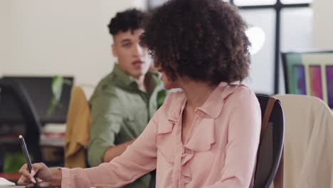 Two-happy-diverse-creative-designers-in-discussion-at-computer-in-casual-office,-slow-motion