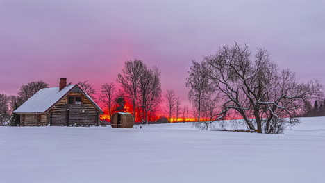 Tiro-De-Lapso-De-Tiempo-Del-Día-Cubierto-De-Nieve-De-Invierno-Frío-En-Un-Paisaje-Rural-Con-El-Amanecer-En-El-Fondo-Sobre-La-Cabaña-De-Madera