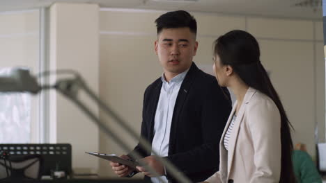 Two-Young-Colleagues-Discussing-While-Walking-In-Office