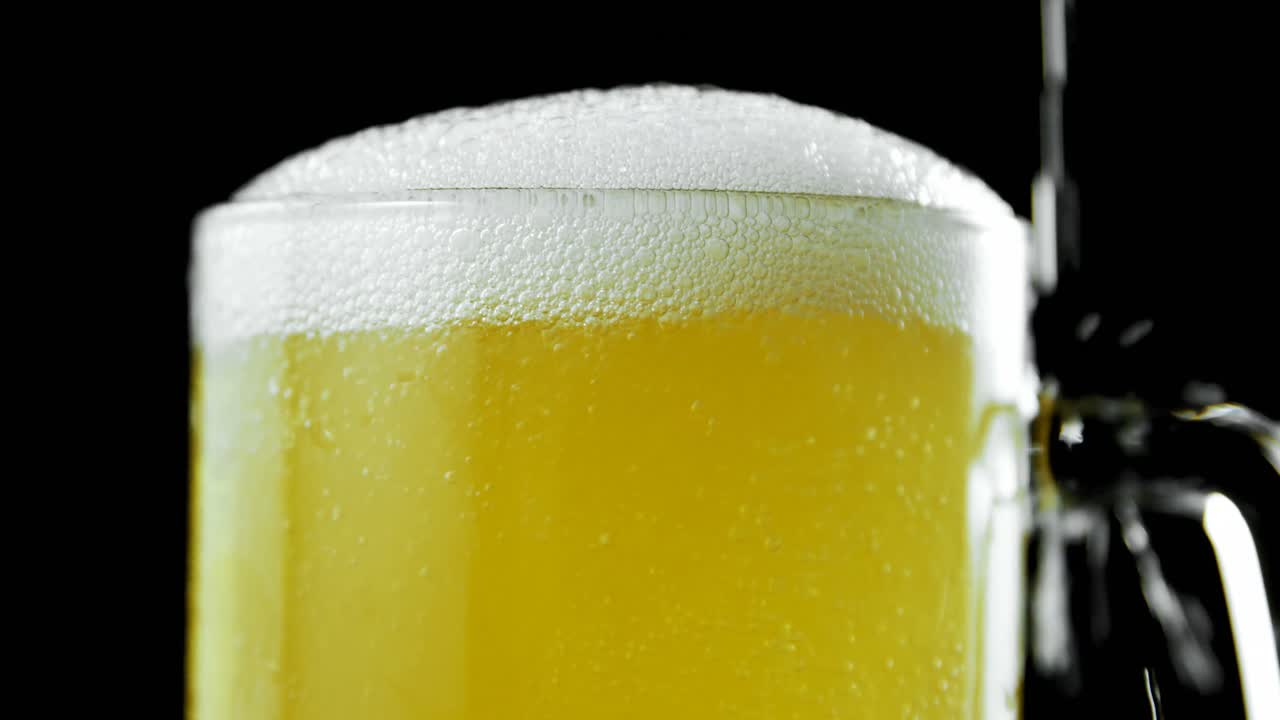 cerveza vertida en una taza de cerveza contra un fondo negro 4k