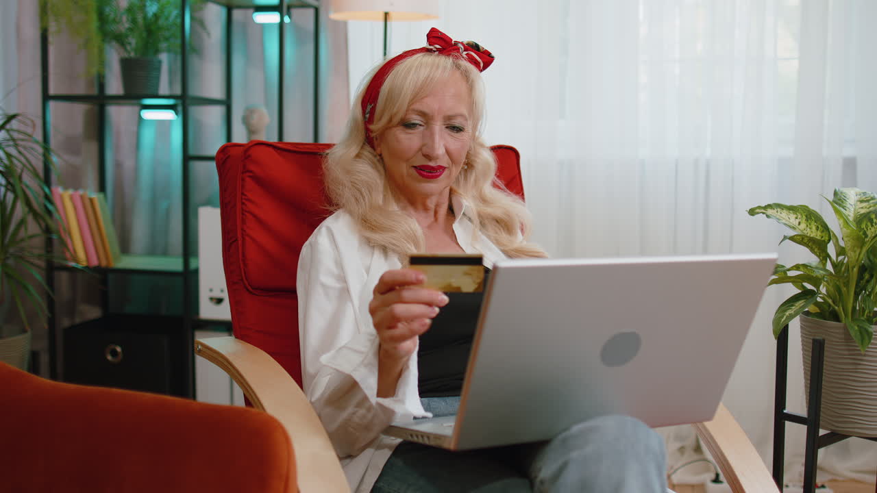пожилая женщина использует кредитную банковскую карту и ноутбук, переводит деньги, делает покупки в интернете.