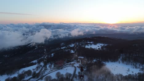 mástiles de transmisor en la cima de una montaña nevada por encima de la inversión de nubes al amanecer