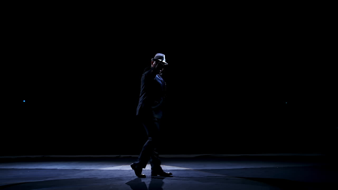Senior man in costume on stage in darkness. Active man in hat dancing on stage during the performance in the theater.