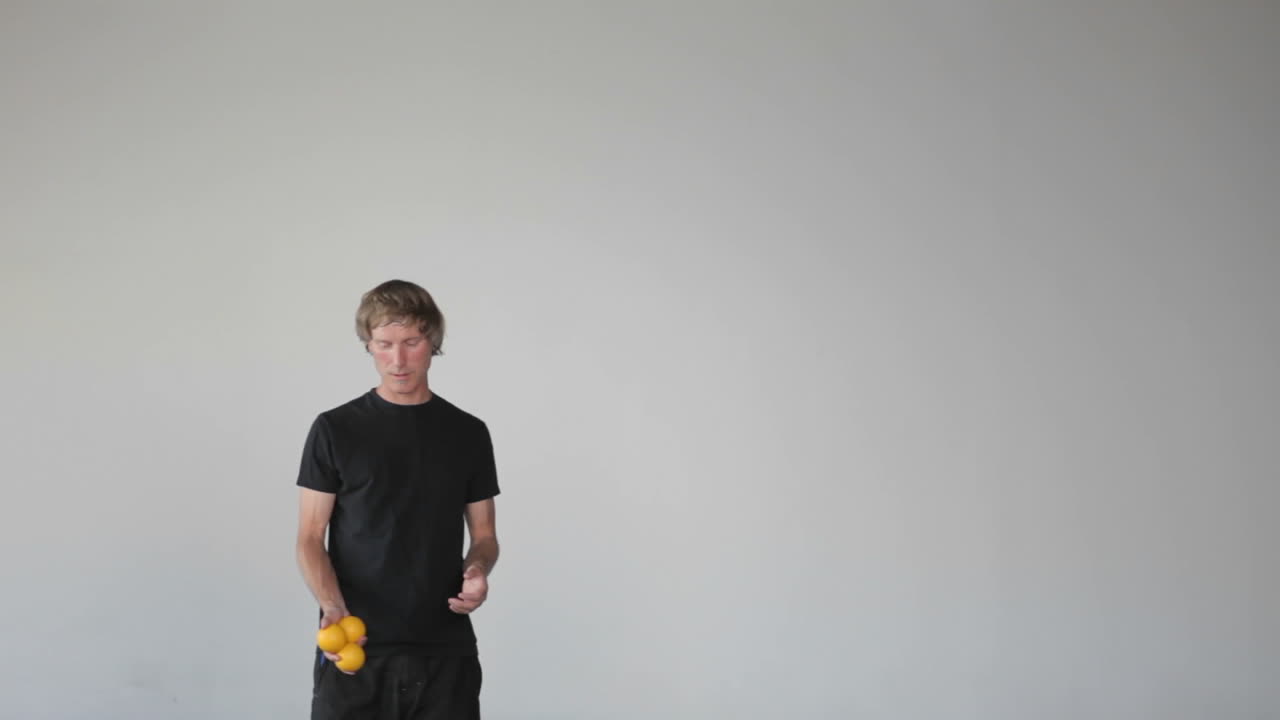 한 남자가 손과 다리를 모두 사용하여 세 개의 주황색 공을 저글링합니다.