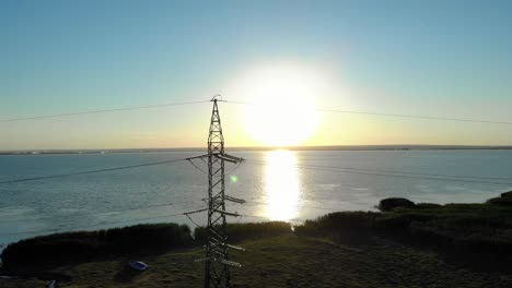 transmission tower with sun reflecting in the water at sunrise in the background