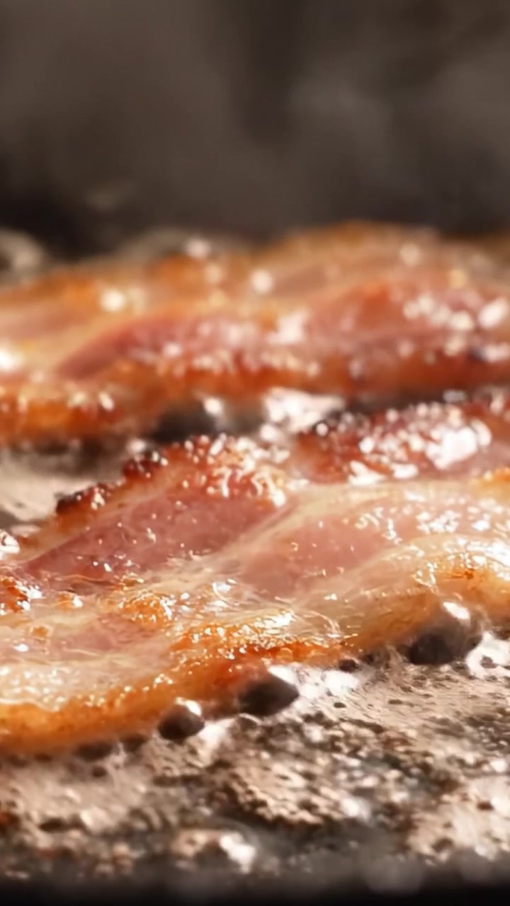 Sydende bacon steger på en pande: Et nærbillede af sprøde strimler i de sidste stadier af tilberedningen, der fanger teksturen og saftigheden før servering