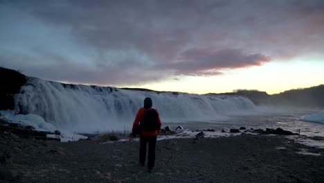 man with backpack walk towards faxi waterfall in iceland