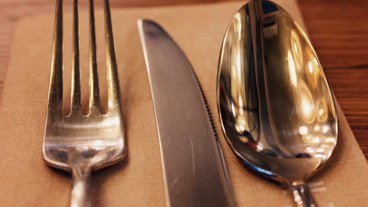 Close up of a fork, knife and a spoon on a napkin on a table at a restaurant