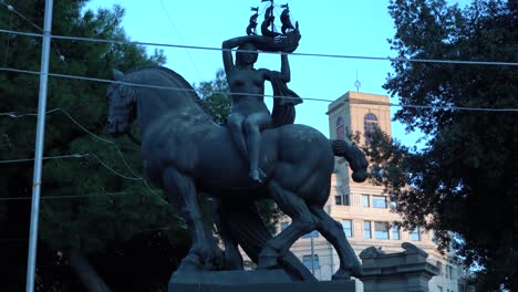 Statue-Eines-Pferdes,-Das-Von-Einer-Frau-Bestiegen-Wird,-Die-An-Einem-Klaren-Abend-Ein-Kleines-Schiff-An-Der-Placa-De-Catalunya-In-Barcelona-Hält