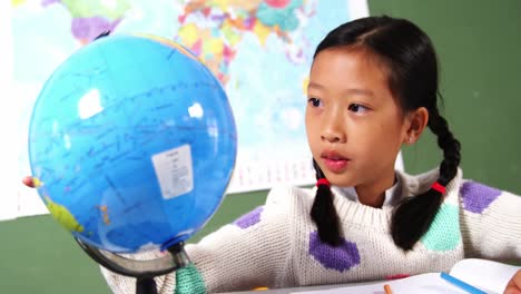 schoolgirl looking at globe in classroom at school