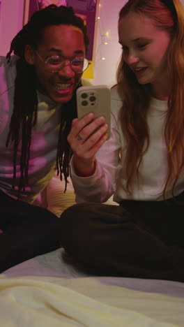 a young couple laughs together while looking at a phone