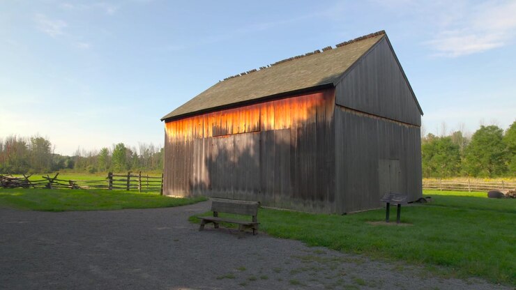 Langsamer Vorwärtsschwenk auf Brigham Youngs Scheune nahe dem Holzrahmenhaus der Familie Smith an der historischen Ursprungsstätte von Joseph Smith für die Kirche Jesu Christi der Heiligen der Letzten Tage in Palmyra, New York