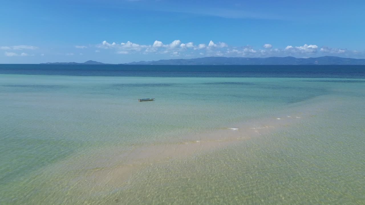 Aerial drone view of Koh Phangan island showing shallow crystal clear turquoise water, tropical coastline and fishing boats anchored along the scenic shore in Thailand