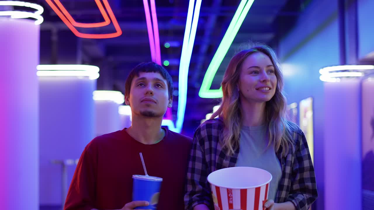 feliz joven y hombre caminando con un cubo de palomitas de maíz y bebida, charlando en el cine