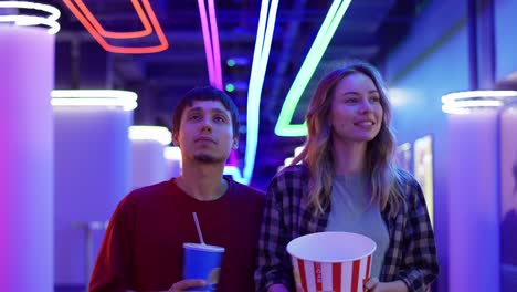 happy young woman and man walking with bucket of popcorn and drink, chatting at cinema