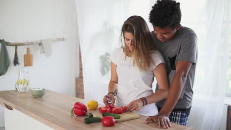 un apuesto hombre africano está abrazando a su novia caucásica mientras la ayuda a preparar comida en la cocina por la mañana. feliz