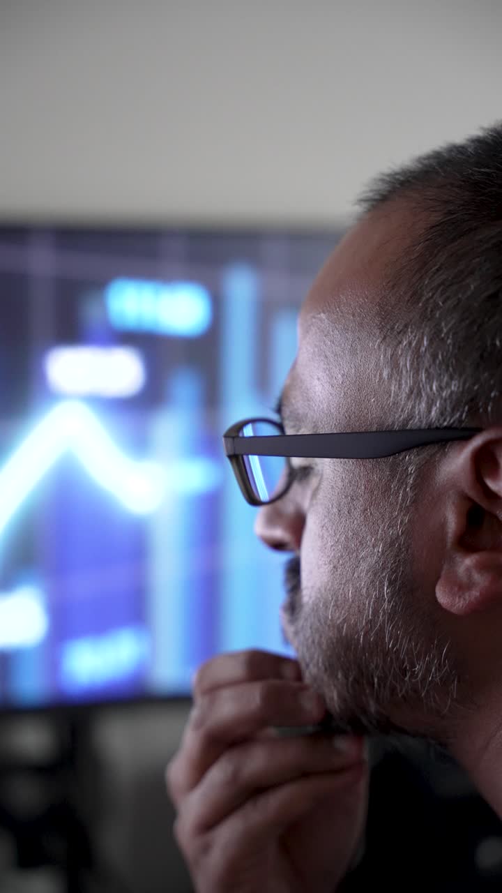 Close-up of man with glasses analyzing stock charts on a screen. vertical video