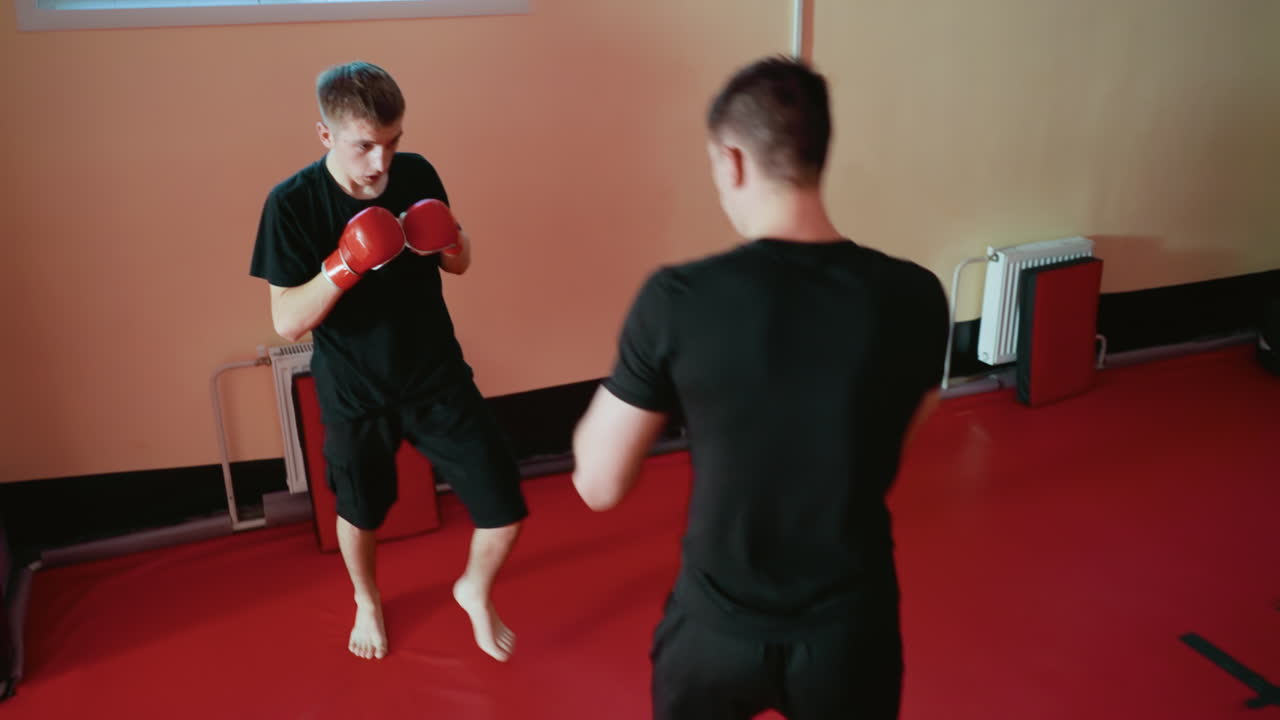 Wrestlers sparring inside gym on red mat, one attacking with punch while opponent defends in focused stance, showcasing combat training, athleticism, strength, intensity, concentration, coordination
