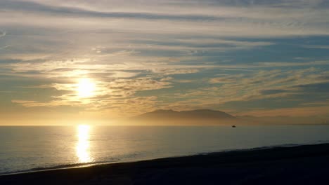 Strandsonnenuntergang-Im-Zeitraffer-Mit-Meereswellen,-Wolken-Und-Bergen-Im-Hintergrund