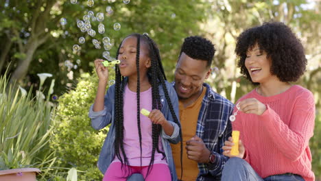 Felices-Padres-Afroamericanos-Con-Su-Hija-Soplando-Burbujas-En-El-Jardín-De-Casa,-Cámara-Lenta