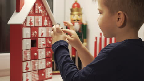 Un-Niño-Feliz-Toma-Dulce-De-La-Forma-De-La-Casa-Del-Calendario-De-Adviento-Con-Cascanueces-De-Navidad-En-El-Fondo