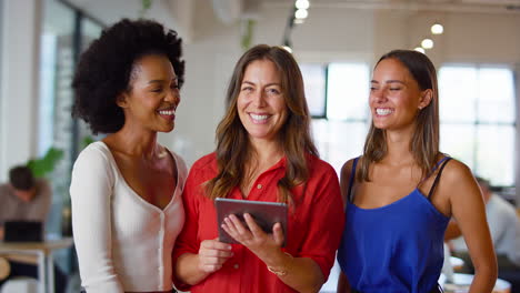 portrait of female multi-cultural business team with digital tablet in modern open plan office