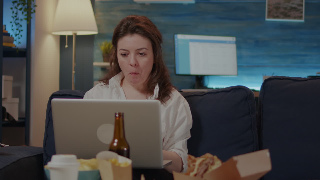 Young woman using laptop on sofa while eating asian food