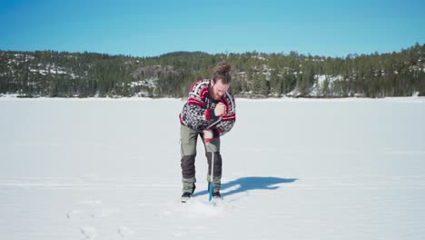 persona perforando un agujero en el lago congelado para la pesca en el hielo durante la soleada temporada de invierno