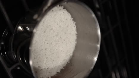 disparo vertical de la persona quitar la tapa de vidrio de la olla brillante con arroz blanco en la estufa